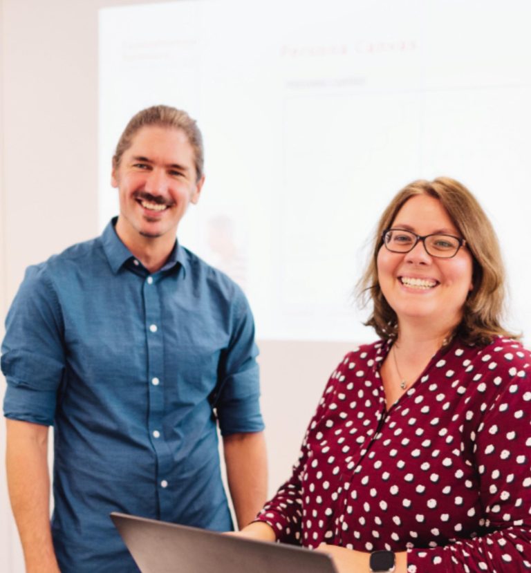 Mann steht an einem Laptop in einem modernen Büro mit Fenstern.